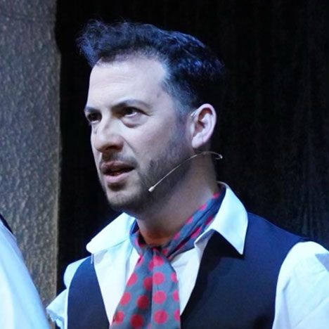 A performer in a waistcoat and red scarf, mid-scene